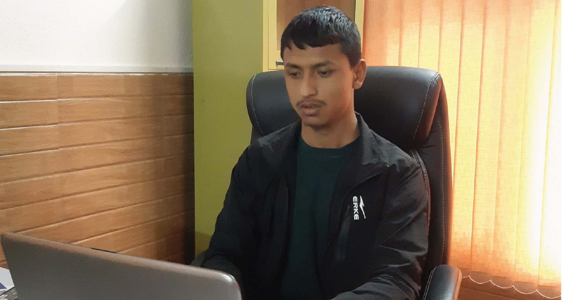 A person wearing green t-shirt and black jacket working in his laptop.